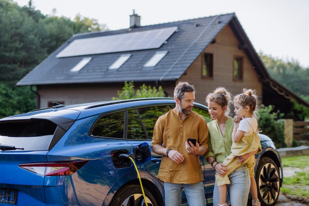 PV-Eigenverbrauch: Familie mit ladendem E-Auto vor Haus mit PV-Anlage.